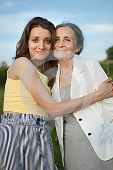 Senior mother with gray hair with her adult daughter looking at the camera in the garden and hugging each other during