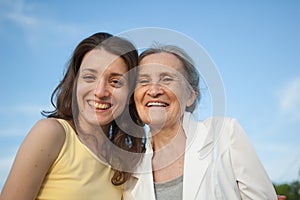 Senior mother with gray hair with her adult daughter looking at the camera in the garden and hugging each other during