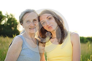 Senior mother with gray hair with her adult daughter looking at the camera in the garden and hugging each other during