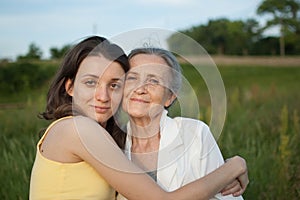 Senior mother with gray hair with her adult daughter looking at the camera in the garden and hugging each other during