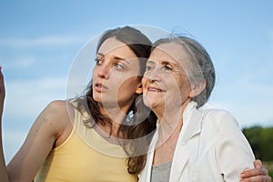 Senior mother with gray hair with her adult daughter looking at the camera in the garden and hugging each other during