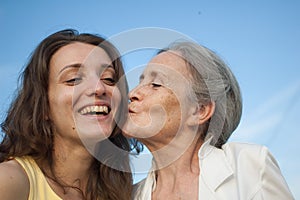 Senior mother with gray hair with her adult daughter looking at the camera in the garden and hugging each other during