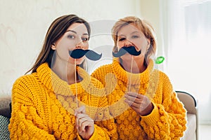 Senior mother and her adult daughter taking selfie with cat using photo booth props at home. Mother`s day concept