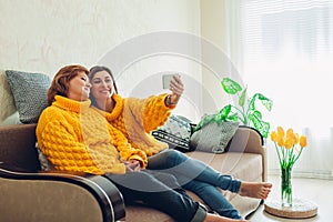 Senior mother and her adult daughter taking selfie using smartphone at home. Mother`s day concept