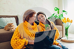 Senior mother and her adult daughter using laptop at home while drinking tea. Mother`s day concept