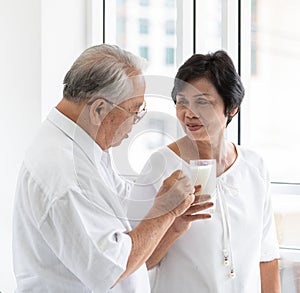 Senior old Asian man and woman lovers holding a glass of milk and drinking together. Idea for the healthcare of elder people