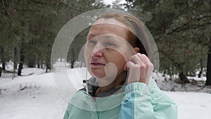 Senior old Caucasian woman puts in earphones before running in the snowy winter park. Close up Front shot