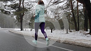 Senior old Caucasian woman running in the snowy park in winter with headphones. Back follow shot