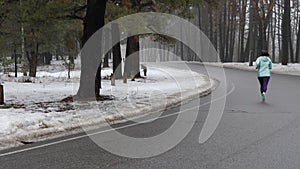 Senior old Caucasian woman running in the snowy park in winter with headphones. Back static shot