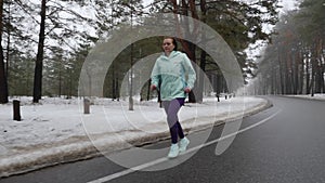 Senior old Caucasian woman running in the snowy park in winter with headphones. Front follow shot