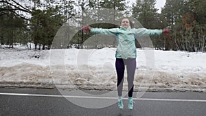 Senior old Caucasian woman warms up jumping before running in the snowy winter park. Front shot