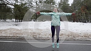 Senior old Caucasian woman warms up jumping before running in the snowy winter park. Front shot. Slow motion