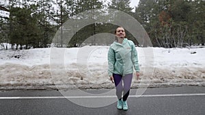 Senior old Caucasian woman warms up jumping before running in the snowy winter park. Front shot. Slow motion