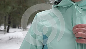 Senior old Caucasian woman  zips her jacket before running in the snowy winter park. Close up Front shot