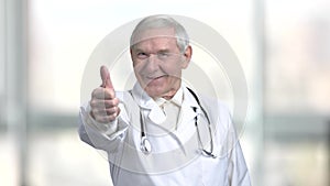 Senior old doctor in white coat and stethoscope shows thumb up.