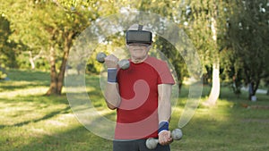 Senior old grandfather man in VR headset helmet making fitness exercises with dumbbells outdoors