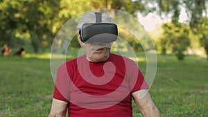 Senior old grandfather man in VR headset helmet making fitness exercises with dumbbells in park