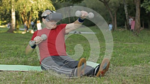 Senior old grandfather man in VR headset helmet making fitness exercises with dumbbells in park