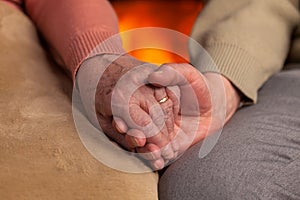 Senior old hands holding in front of fireplace