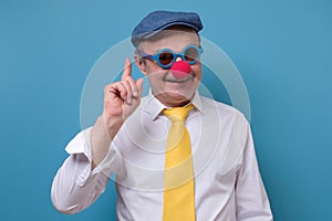 Senior old man with clown nose smiling pointing uo giving advice