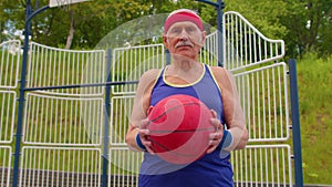 Senior old man grandfather athlete posing playing with ball outdoors on basketball playground court