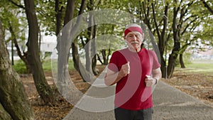 Senior old man running, working out cardio in park and using bluetooth earphones, listening music