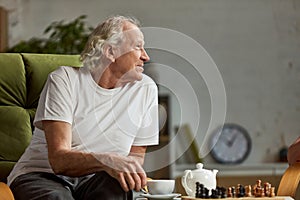 Senior, old, retired man sitting on chair at home, playing chess, talking. Leisure time and hobby. Home interior