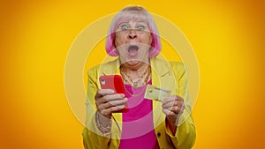 Senior old stylish granny woman using credit bank card and smartphone purchases online shopping