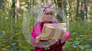 Senior old tourist grandmother woman lost and looking at map while having walk in wood outdoors