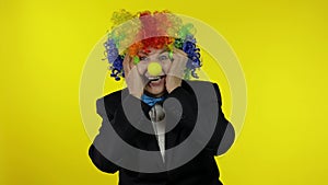 Senior old woman clown in colorful wig looks surprised shocked. Amazement