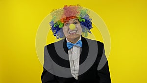 Senior old woman clown in colorful wig smiling, making silly faces, fool around