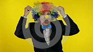 Senior old woman clown in colorful wig smiling, making silly faces, fool around