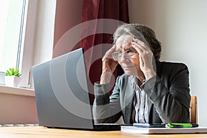 Senior old woman female sit desk, home office online notebook laptop work business distance freelancer, tired bored