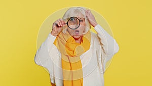 Senior old woman holds magnifying glass near face looking at camera with big zoomed eye, analyzing