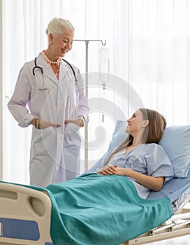 A senior older female doctor standing in an elegant pose put hands in pocket, and smile with kindness taking photos with a younger