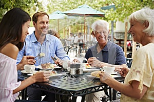 Senior Parents With Adult Children Enjoying Meal At Outdoor Cafe