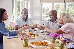 Senior Parents With Adult Offspring Making Toast Sitting Around Table For Family Meal