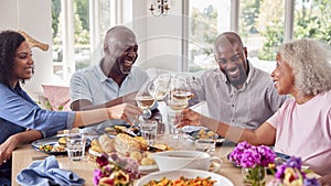 Senior Parents With Adult Offspring Making Toast Sitting Around Table For Family Meal