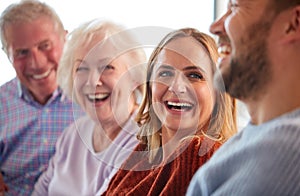 Senior Parents With Adult Offspring Sitting On Sofa At Home Talking And Laughing