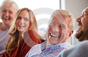 Senior Parents With Adult Offspring Sitting On Sofa At Home Talking And Laughing