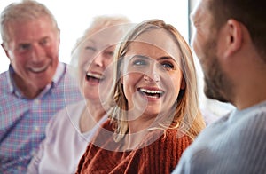 Senior Parents With Adult Offspring Sitting On Sofa At Home Talking And Laughing