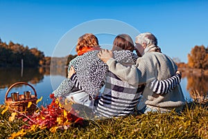 Senior parents relaxing by autumn lake with their adult daughter. Family values. People having picnic