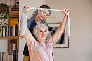 Senior patient doing exercise with elastic band at home with personal trainer