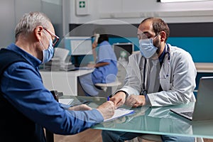 Senior patient signing consultation report in medical office with doctor