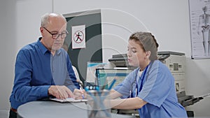 Senior patient talking to nurse at reception counter in health center