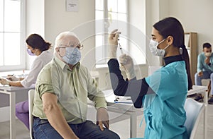 Senior patient waiting to get a shot and looking at young doctor getting the vaccine ready