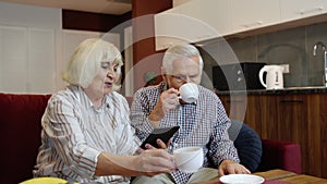 Senior pensioner couple with digital tablet pc computer at home. Resting on sofa in cozy living room