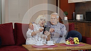 Senior pensioner couple with digital tablet pc computer at home. Resting on sofa in cozy living room