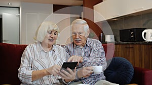 Senior pensioner couple with digital tablet pc computer at home. Resting on sofa in cozy living room