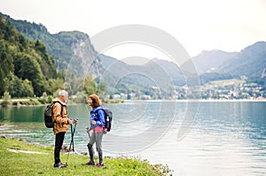 A senior pensioner couple hikers standing by lake in nature, talking.